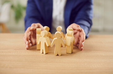 Close up of a man entrepreneur wearing suit protecting wooden toy people figures by hands standing...