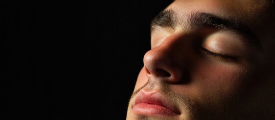 Obraz premium Sleepy Young Male Portrait with Closed Eyes Against Dark Black Background Featuring Expansive Copyspace for Text and Design Elements