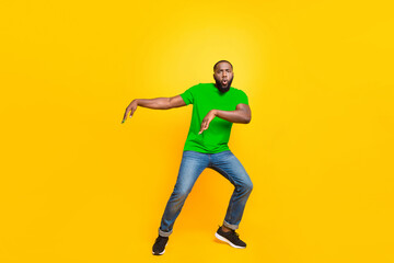 Full length body size photo of black man dancing with face serious while isolated with yellow background