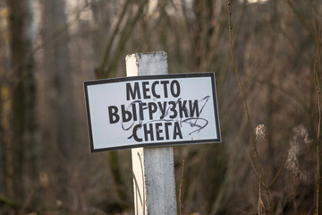 A sign on a wooden pole with the inscription in Russian "Snow dumping area" against the background of trees.