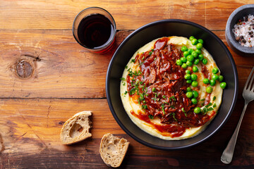 Mashed potatoes with beef meat, green peas in bowl and grass of red wine. Wooden background. Copy space. Top view.
