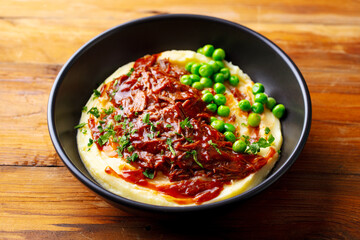 Mashed potatoes with beef meat and green peas in bowl. Wooden background. Close up.