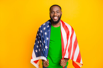 Photo of black american man patriot having put on american flag while standing isolated with yellow background