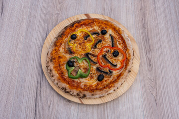 Paris, France - 11 06 2023: Italian culinary Still Life. A vegetarian pizza with red pepper, green pepper, yellow pepper, onions and olives seen from above and placed on a wooden tray.