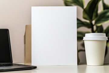 Fototapeta premium close-up of blank poster placed on neutral desk surrounded by laptop and coffee cup for professional feel