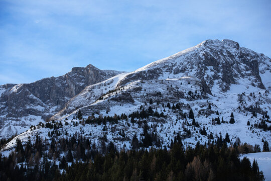 Montagnes enneig&eacute;es sous les nuages d'hiver dominant une vall&eacute;e bois&eacute;e et enneig&eacute;e &agrave; la lumi&egrave;re rasante du matin.