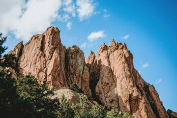 Fototapeta premium A dynamic photograph of a mountain range, shot from a low angle to emphasize the towering peaks against the bright blue sky. The rugged terrain is accentuated by the contrast between light and shadow