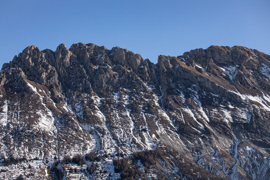 Montagne rocheuse presque sans neige au printemps avec sapins et m&eacute;l&egrave;zes sur son flanc sous un ciel bleu..