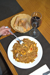 A horizontal shot featuring a person holding a white plate of freshly prepared Fideu&agrave;