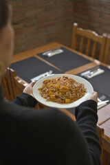A horizontal shot featuring a person holding a white plate of freshly prepared Fideu&agrave;. 