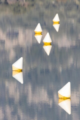 Reflections of white buoys with yellow bases floating on a calm, still lake. Minimalist composition...