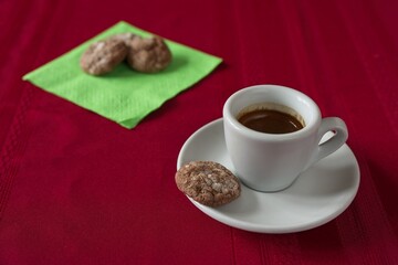 A shot of espresso with a group of espresso coin cookies on a green napkin.