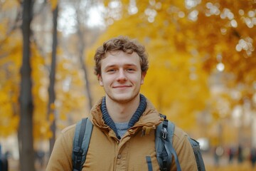 Smiling young man in cozy autumn attire amidst vibrant yellow trees in park setting, perfect for autumn themed design and text overlay.