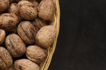 Walnuts in a wicker basket on a dark wooden background. Nuts in an oval basket, top view. Heap of walnuts in shells, close-up, background. Healthy eating. Harvest, agriculture