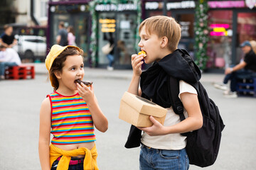 Kids eating colorful sweet and tasty donuts. Children snacking on unhealthy food outdoors.