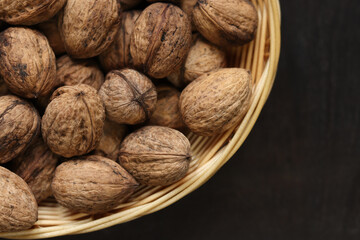 Walnuts in a wicker basket on a dark wooden background. Nuts in an oval basket, top view. Heap of...