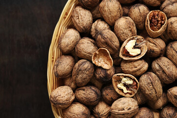 Walnuts in a wicker basket on a dark wooden background. Nuts in an oval basket, top view. Heap of...
