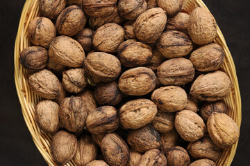 Walnuts in a wicker basket on a dark wooden background. Nuts in an oval basket, top view. Heap of walnuts in shells, close-up, background. Healthy eating. Harvest, agriculture