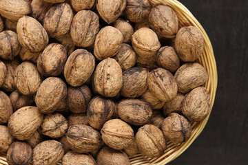Walnuts in a wicker basket on a dark wooden background. Nuts in an oval basket, top view. Heap of walnuts in shells, close-up, background. Healthy eating. Harvest, agriculture