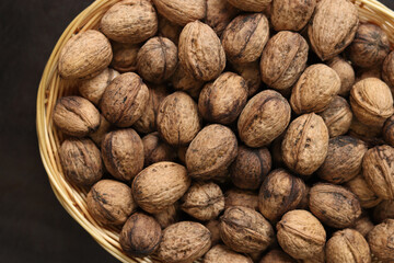 Walnuts in a wicker basket on a dark wooden background. Nuts in an oval basket, top view. Heap of walnuts in shells, close-up, background. Healthy eating. Harvest, agriculture