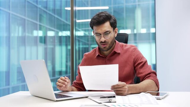 Confused businessman unhappy with financial results checking documents on computer sitting at workplace in business office. Frustrated male accountant is unhappy reading document with bad indicators