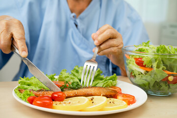 Asian elderly woman patient eating salmon stake and vegetable salad for healthy food in hospital.