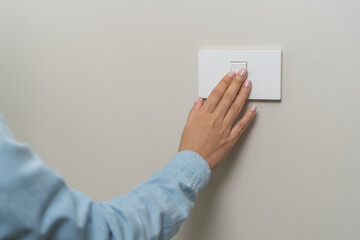 Asian young woman hand turn off on lighting switch at home room. Finger pushing light switch turn...