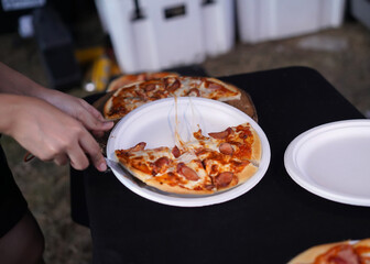 woman hand scoop up slice pizza from a wooden cutting board place on a white dish on a black table.