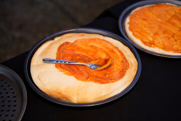 Prepare the pizza. Spread sauce on bread with spoon on a black table.