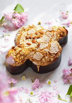 Сolomba pasquale - Italian sweet Easter bread or cake with almonds and powdered sugar and candied fruits. The baked dove is a symbol of Christ and the Easter holiday, pink flowers. Bright light, eco 