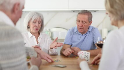 Cheerful friendly company of men and women sitting at kitchen table and enjoying the poker game. Friends play a card game at home. Evening entertainment concept