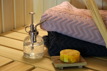 glass bottle with metal spray, towels, soap and bamboo massage whisk in sauna