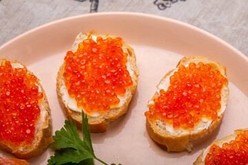 Canapes with red caviar and salted salmon on a plate decorated with cilantro