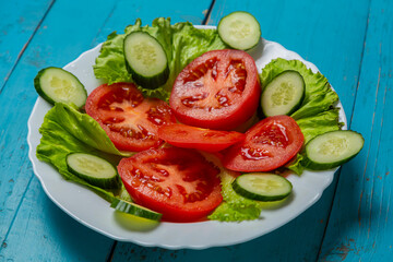 Salad, cucumbers and tomatoes in circles in a white plate on a blue
