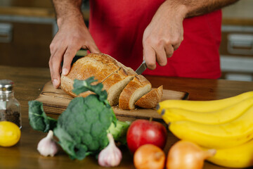 Close up of hands cutting a slice of bread. Male hands cutting bread on wooden board