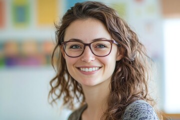 Obraz premium A cheerful young woman with curly hair and glasses shares a radiant smile, standing in a bright, artistic environment filled with colorful patterns in the background.