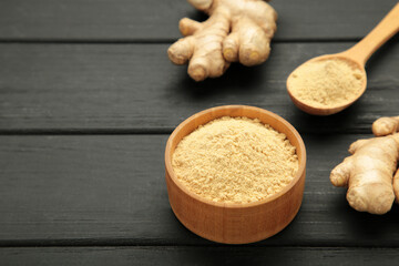 Wooden spoon with dried ginger powder and fresh ginger root on black wooden background. Top view