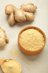 Ginger powder on bowl with fresh ginger root on light background. Vertical photo