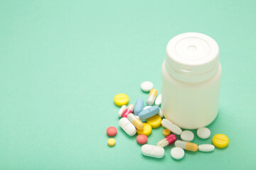 Assorted pharmaceutical medicine pills, tablets and capsules and bottle on mint background.