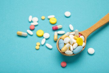 Assorted pharmaceutical medicine pills, tablets and capsules on wooden spoon on blue background.