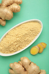 Ginger powder on white plate with fresh ginger root on mint background. Top view