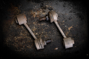 Two worn-out car stabilizer links on a textured rusty surface. Perfect for themes related to automotive repair, vehicle maintenance, or mechanical engineering