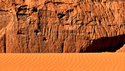 Red sand forming ripples, rocks detail in the background, Sahara.