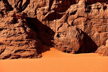 Red sand forming ripples, rocks detail in the background, Sahara.