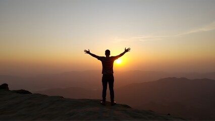 Silhouette of a man standing on a mountain peak with arms wide open, embracing the sunrise. The peaceful orange hues highlight freedom, nature, and new beginnings.