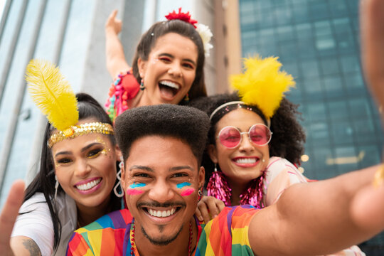 Joyful friends celebrating Brazilian Carnival in colorful costumes outdoors. Cheerful group of young adults with vibrant makeup enjoying urban Carnaval in the street