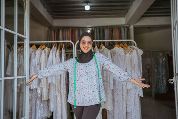 A cheerful woman welcomes customers in a bridal boutique filled with elegant gowns.
