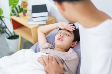 Fototapeta premium An Asian man is taking care of his son who is sleeping or resting on the bed.