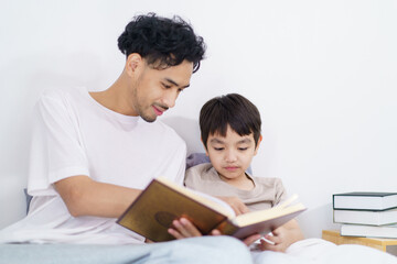 Asian father and son are learning the Quran together in morning.