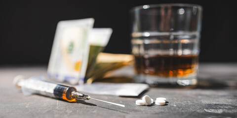 White drugs, narcotic pills, an alcoholic drink in a glass, syringe with a dose of heroin, cocaine powder, and US dollar bills on a dark background. Concept of addiction and bad habits